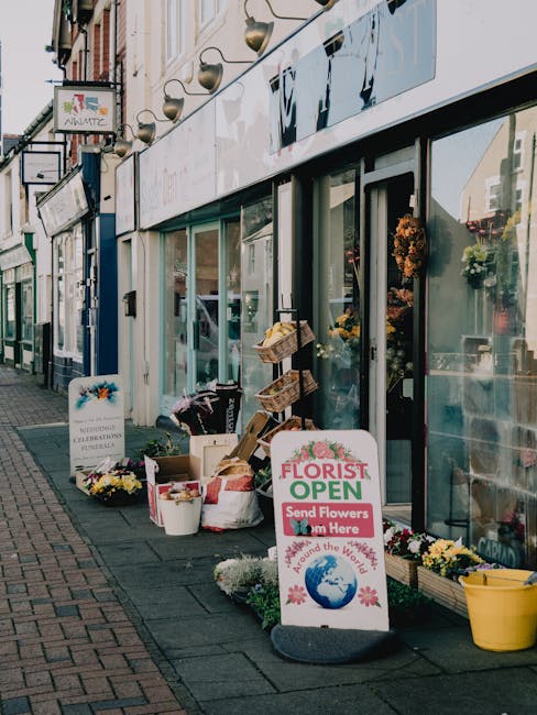 Exterior view of Northwood High Street florist, Flowers Northwood, showcasing an open storefront with large glass windows revealing colorful floral arrangements inside. Outside the shop, there are sev