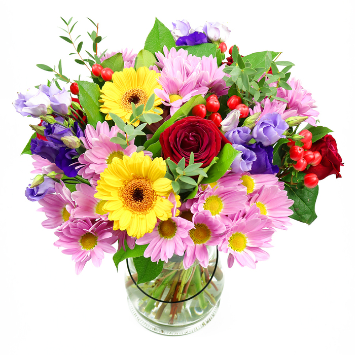 A lush bouquet brimming with colour and texture stands proudly in a clear glass vase, its silhouette rounded and full against a spotless white background. The composition is anchored by luxurious deep red roses placed at the centre, their rich, velvety petals spiralling inward to create a sense of depth and heartfelt emotion. Just off-centre, two vibrant yellow gerbera daisies radiate outward, their evenly spaced petals framing dark brown-orange centres that bring a warm, sun-kissed glow, echoing the brightness of a walk through Northwood's leafy streets on a clear day. Enveloping this central cluster are plentiful pink daisies or chrysanthemums, each with many fine petals and a tiny yellow centre, forming a soft, pastel canopy that adds both volume and gentle charm. Intertwined among the pinks, lisianthus blooms in shades of purple and lavender unfurl their bell-shaped blossoms, some fully open, others still partially closed, contributing a graceful, slightly whimsical note. Tucked between petals, small clusters of glossy red hypericum berries catch the light, their round, bead-like shapes adding a tactile contrast to the more delicate flowers. A thoughtfully chosen mix of greenery supports and frames the blooms: broad, deeper green leaves give the structure a grounded feel, while lighter, slender stems and sprigs extend outward, lending a sense of natural movement and freshness. Through the side of the glass vase, the neatly trimmed green stems can be seen standing in clear water, reflecting the skilled hand of a local florist. Created with homes and celebrations in Northwood in mind, this arrangement feels ideal for marking special occasions, sending thanks, or simply brightening a living room with a burst of garden-inspired beauty.
